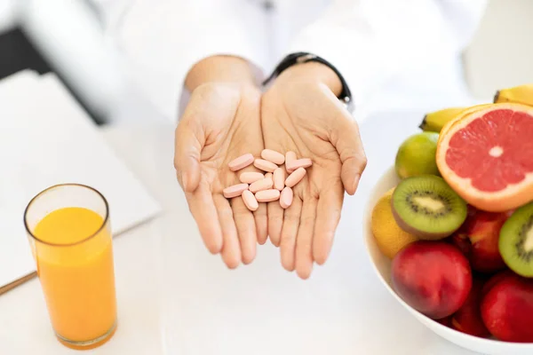大人のヨーロッパの女性医師の栄養士有機果物やジュースとテーブルの白いコートでオフィスクリニックで手に錠剤を保持しています 推奨健康管理 適切な栄養 — ストック写真