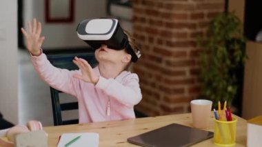 Yenilikçi temel öğrenme. Sanal gerçeklik gözlüğü takan sevimli küçük kız fütüristik dersin tadını çıkarıyor, başını çeviriyor ve görünmez tuşlara basıyor, çekim takip ediyor, yavaş çekim, serbest alan