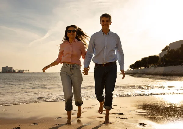 快乐的中年夫妇夏天在海滩上奔跑 快乐的中年男人和女人牵着手 微笑着 丈夫和妻子在户外约会时快乐地在一起 复制空间 — 图库照片