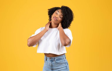 Bin yıllık hüzünlü zenci kadın boynu ağrıyordu, turuncu stüdyo arka planında izole edilmişti. Yorgun insan duyguları, kas spazmı, aşırı çalışma ve teklif, sağlık sorunları