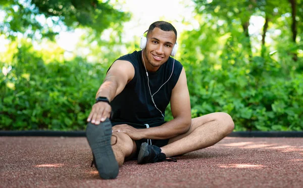 Позитивный Привлекательный Африканский Спортсмен Спортивной Одежде Наушниках Растягивающих Ноги Бега — стоковое фото