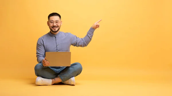 Онлайн Пропозиція Усміхнений Азіатський Чоловік Сидить Підлозі Ноутбуком Вказує Копіювальний — стокове фото