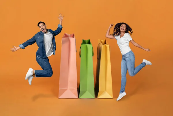 ショパホリックだ 喜び中東配偶者お祝い偉大なショッピング ジャンプ近くに巨大なバッグ笑顔でカメラでオレンジ背景 コラージュ バイヤーのカップルの広告販売の提供近くの買物客 — ストック写真