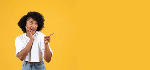 陽気ショックを受けた若い黒人女性のカジュアルなオープン口で コピースペースでポイント指 オレンジのスタジオの背景 パノラマに孤立した 巨大な販売 驚きの反応 人間の感情 広告やオファー — ストック写真