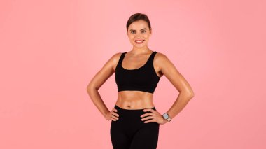 Vücut şekillendirme. Spor Giyim 'deki Genç Atletik Kadın Ellerini Belde Tutuyor ve Kamera' ya Gülümsüyor, Güzel Neşeli Sporcu Kadın Pembe Stüdyo Arkaplanının Üzerinde Tek Başına Duruyor, Boşluğu Kopyala