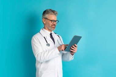 Modern sağlık konseptinde yapay zeka yapay zekası. Mutlu, gri saçlı orta yaşlı doktor gözlük takıyor modern dijital tablet kullanıyor, mavi arka plan, kopyalama alanı kullanıyor.