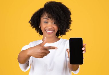 Milenyum siyahi bayanın boş ekranlı telefonu göstermesine sevindim. Portakal rengi stüdyo arka planda izole edilmiş, yakın çekim. Reklam ve teklif, web sitesi, uygulama ve blog tavsiyesi