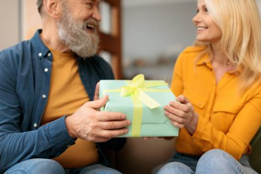 Doğum günü, yıldönümü hediyesi. Romantik son sınıf çifti ellerinde paketlenmiş hediyeler, karı koca, aile tatilini evde kutluyor. Ellerindeki kutuya odaklan, kırpılmış atış.