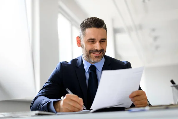 stock image Positive middle aged businessman working with papers at workplace in office, entrepreneur man reading financial reports and taking notes, enjoying company growth and smiling