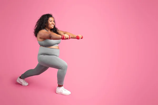 黒ぽっちゃり女性ダンベルを保持し 肺の運動を作る ピンクのスタジオの背景に足をトレーニング コピースペース ボディケアと減量のワークアウト — ストック写真