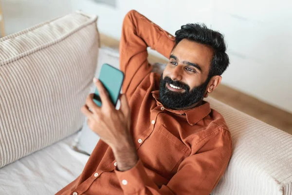 Glad Arabiska Man Som Håller Mobiltelefon Lutar Sig Mot Soffan — Stockfoto