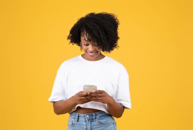 Bin yıllık siyahi bir kadın telefonda sohbet ediyor, sosyal ağlar yazıyor, mesajlar okuyor, turuncu stüdyo geçmişinde izole edilmiş. Satış, reklam ve uygulama, iyi haberler ve blog