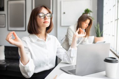 Sakin genç bayan yönetici ofis meditasyonunu laptopun önünde dinlenmek için yapıyor. Çalışan dikkatli bir kadın iş kavramında stres olmadan rahatlıyor.