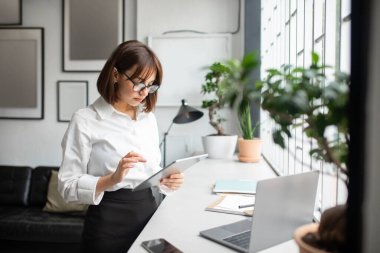 Ofiste çalışan serbest çalışan ve dijital tablet kullanan, internetten e-postalarına cevap veren, arkadaşlarıyla mesajlaşan ya da iş uygulamalarına göz atan, serbest alan kullanan bir kadın.
