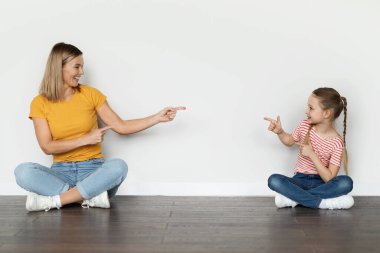 Neşeli genç bir anne ve küçük bir kız yerde oturmuş birbirlerini işaret ediyorlar, pozitif beyaz bir anne ve tatlı bir çocuk evde birlikte eğleniyorlar, 