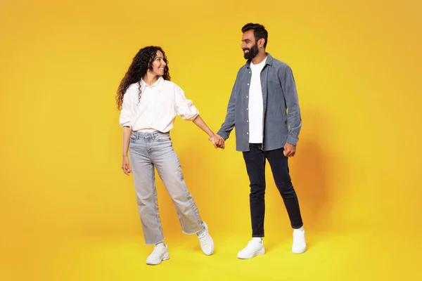 恋愛関係 幸せな千年紀のアラブカップルが手を取り合って歩き 黄色のスタジオの背景 完全な長さにわたって互いに笑顔 男と女が一緒にポーズをとる 家族愛 — ストック写真