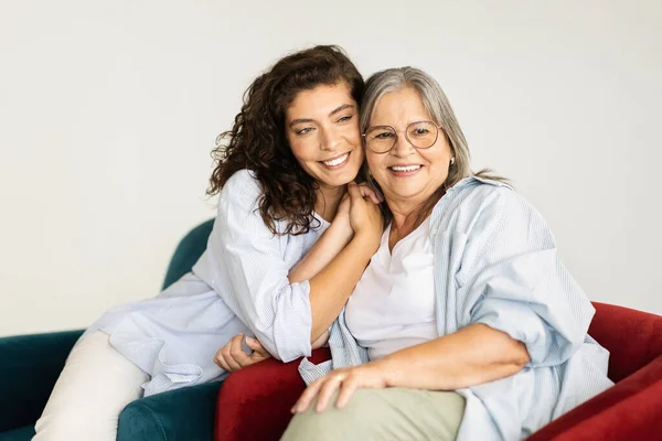 快乐的老年妇女拥抱着千禧年淑女 享受着看望父母的乐趣 孤独在客厅的白色工作室背景中 家庭支助 女性一代 母女关系 — 图库照片