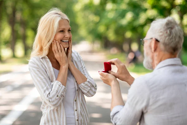 大人の愛 ロマンチックなシニア紳士は 彼らが夏の公園で歩いている間 喜びの女性に結婚を提案婚約指輪を持つ幸せな興奮した女性の屋外に提案をします グレーの髪の男 — ストック写真
