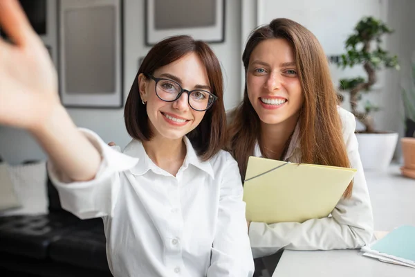 stock image Two european female friends colleagues workers taking selfie, looking and smiling at camera during break in office, business people talking on video call