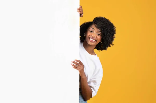オレンジのスタジオの背景に隔離された無料のスペースと大きなバナーの後ろにカジュアルな素敵な千年黒の女性 人間の感情 広告とオファー 良いニュース — ストック写真