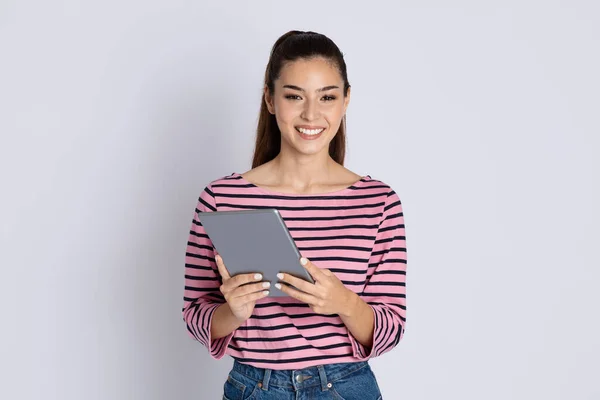 幸せなかなりブルネット長い髪ミレニエルの女性は灰色のスタジオの背景に現代のPcデジタルタブレットを使用してカジュアルな衣装を着て 最新のアプリをチェックし オンラインで動作し コピースペース — ストック写真