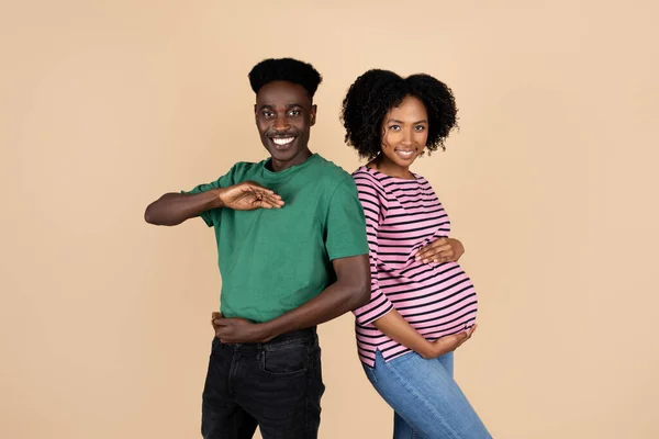 笑千年的非洲裔美国丈夫手里拿着空虚的空间 大肚子的女人玩得开心 享受怀孕的快乐 被米色背景隔离 对子女的期望 — 图库照片
