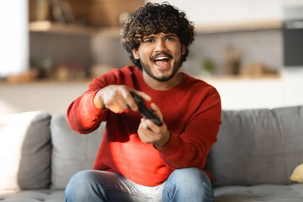 网上竞争概念 兴奋的印度年轻人在家里玩电子游戏 快乐的东方男人拿着控制台操纵杆 游戏玩家坐在客厅沙发上 复制空间的肖像 — 图库照片