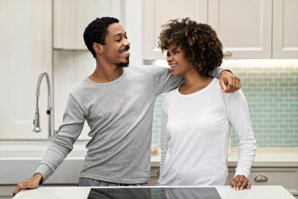 美しいアフリカ系アメリカ人のカップル千年の男性と女性快適な家庭用ポージングを身に着けていますキッチンで テーブルのそばに立って 包含し お互いを見て 一緒に時間を楽しんで配偶者 — ストック写真
