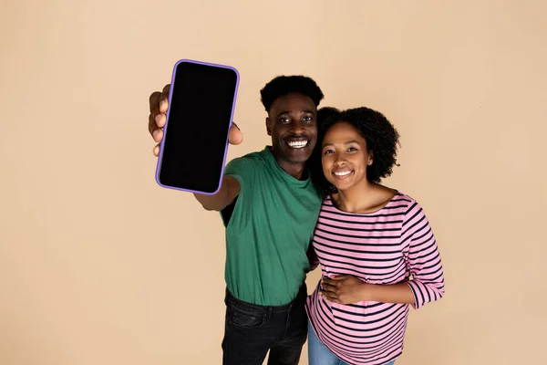 何百万人ものアフリカ系アメリカ人の男性と女性が笑顔で ベージュの背景に隔離された空白の画面を持つ大きな腹のショー電話 妊娠計画のためのウェブサイトの勧告 アプリ 赤ちゃんを期待 — ストック写真