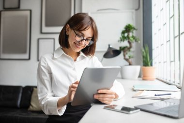Çevrimiçi çalışan kendine güvenen Avrupalı iş kadını, yatırım tabletine yazıyor veya modern ofis içi müşterilerle sohbet ediyor. Uzaktan iş uygulaması, finansman pazarlaması