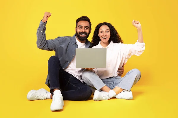 オンライン運 ラップトップコンピュータを使用して幸せな中東配偶者とジェスチャーはい 喜びとニュース 黄色の背景に座っている広告ウェブサイトを祝う拳を振る スタジオショット — ストック写真