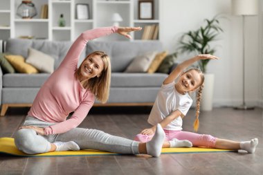 Gülümseyen anne ve küçük kız evde spor paspası üzerinde egzersiz yapıyor, kollarını kavuşturup kameraya bakıyor, anne ve tatlı bayan chid ev içi eğitimden, boş alandan keyif alıyorlar.