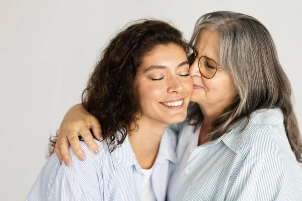 快乐的欧裔老年妇女拥抱 亲吻千禧年淑女 孤身一人在白色工作室的背景下 亲密相拥 家庭支助 女性一代 母女关系 — 图库照片