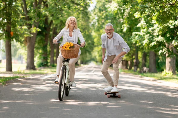 现代养恤金领取者 快乐的老夫妇在公园骑自行车和滑板 快乐的成熟男人和女人一起在户外玩乐 享受退休后的积极生活方式 复制空间 — 图库照片