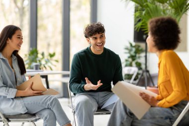 Takım çalışması konsepti. Uluslararası arkadaş öğrenciler birlikte eğitim projelerini konuşuyor ve tartışıyorlar, birlikte çalışma alanındaki sandalyelerde oturuyorlar.