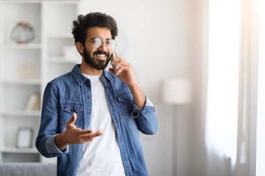 Evde cep telefonuyla konuşan yakışıklı Hintli adamın portresi oturma odasındaki pencerenin yanında duran neşeli, genç ve neşeli, hareketli sohbetin tadını çıkartan doğulu adam.