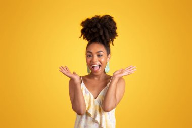 Bin yıllık Afro-Amerikan elbiseli bayanın sarı arka planda ve stüdyoda izole bir şekilde kollarını yana açmasına sevindim. Harika haberler, moda yaşam tarzı, sürpriz tepkiler, tatil, reklam ve teklif