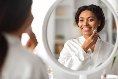 Günlük Skincare. Çekici siyah bayan pamuklu pedlerle deriyi temizliyor, güzel Afro-Amerikan kadın makyajdan yüzünü temizliyor ve aynaya bakıyor, boş alanla yakın çekim.