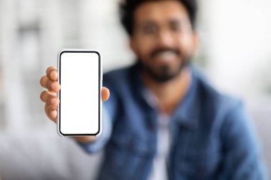 Kamerada boş beyaz ekranlı gülümseyen Hintli adam, Yeni Mobil Uygulamayı Öneren Mutlu Doğulu genç adam ya da Evdeki Kanepede otururken Web Sitesi, Seçici Odaklanma, Model