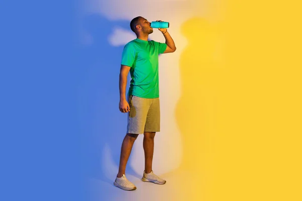 水份和体重减轻 年轻的黑人运动员从水壶中喝水的全长 在蓝黄相间的训练中喝水的时间 自由空间 — 图库照片