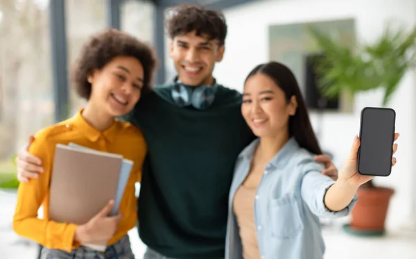 三位快乐多样的学生朋友拥抱着 一位亚裔女士展示着手机空白屏幕 广告教育应用 站在大学走廊 — 图库照片