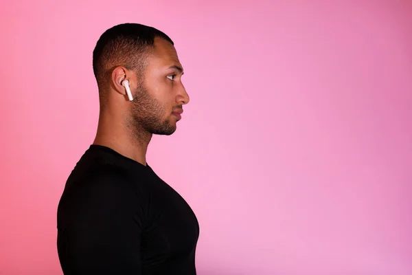 健身运动员名单 配戴耳塞的黑人的侧视图肖像除了看复制空间外 还听着粉红工作室背景上的音乐 持有无线耳机的年轻人简介 — 图库照片