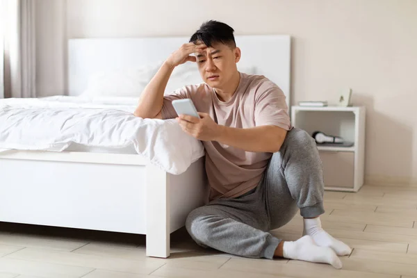 不幸な落ち込んでハンサムな中国のビジネスマンを使用して電話 床に居心地の良い白い寝室のベッドの横に座って 危機の間にビジネスの難しさを経験し スペースをコピー — ストック写真