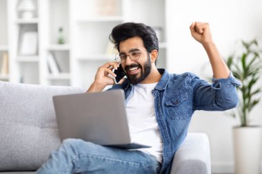 Evde cep telefonu ve dizüstü bilgisayarı olan neşeli Hintli adam bilgisayar ekranına bakıp Joy 'a yumruk atan heyecanlı Doğu' lu genç adam internetten zaferi kutluyor, yakın plan çekimleri yapıyor.