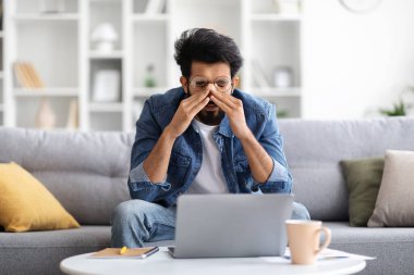 Evde dizüstü bilgisayarla çalışırken yorgun hisseden, oturma odasında koltukta otururken Doğu Erkek Köprüsü 'ne masaj yapan, bilgisayar kullandıktan sonra yorulan genç Hintli adam,