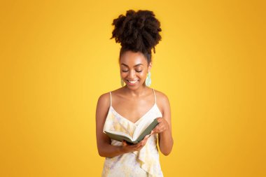 Gülümseyen bin yıllık Afro-Amerikan bayan kitap okuyor, boş zamanın, ödevin, sarı arka planda izole edilmiş stüdyonun tadını çıkarıyor. Reklam ve teklif, öğrenim, hobiler, eğitim ve günlük planlama