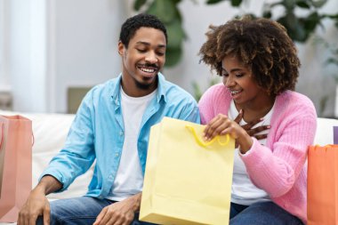 Mevsim indirimi, Kara Cuma, perakende. Evdeki kanepede oturmuş, alımları kontrol eden, gündelik giysiler içinde mutlu, genç, güzel siyah bir çift. Heyecanlı Afrikalı Amerikalı kadın alışveriş çantasına bakıyor.