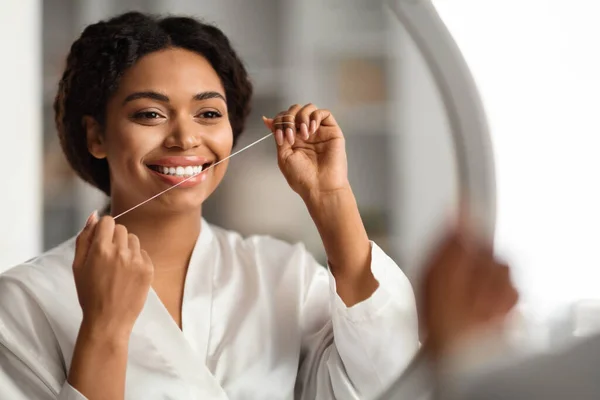 口腔卫生 年轻黑人妇女用假牙刷牙的特写 漂亮地微笑着 用螺纹清洁着非洲裔美国女性的牙齿 而站在镜子前 自由自在的空间 — 图库照片