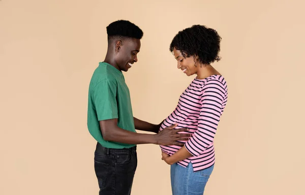 积极的千年非洲裔美国男人抱着大肚子的女人 感觉运动的孩子 孤立在米色的背景下 工作室 新生儿 家庭关系 不孕症治疗 — 图库照片