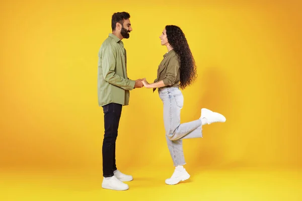 ロマンチックな愛 黄色のスタジオを背に立ち女性に提案する幸せな中東のカップルが手を取り合って笑っています フルレングスショット サイドビュー — ストック写真